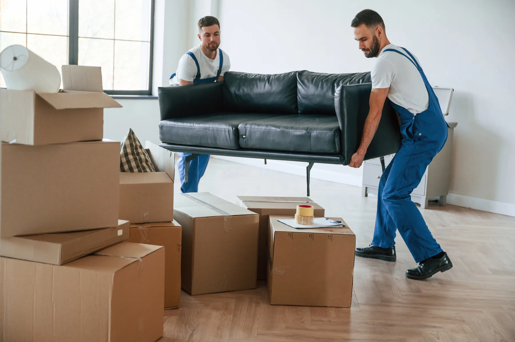 Zwei Mitarbeiter tragen ein Sofa durch eine Wohnung